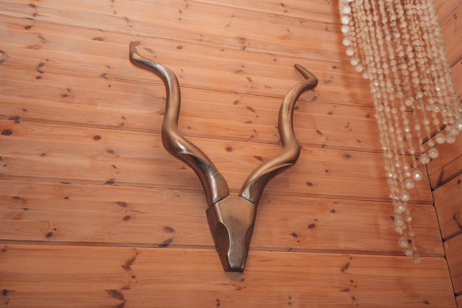 Gewölbeformige Hirschgeweih-Skulptur an Holzwand mit Kristallhänger