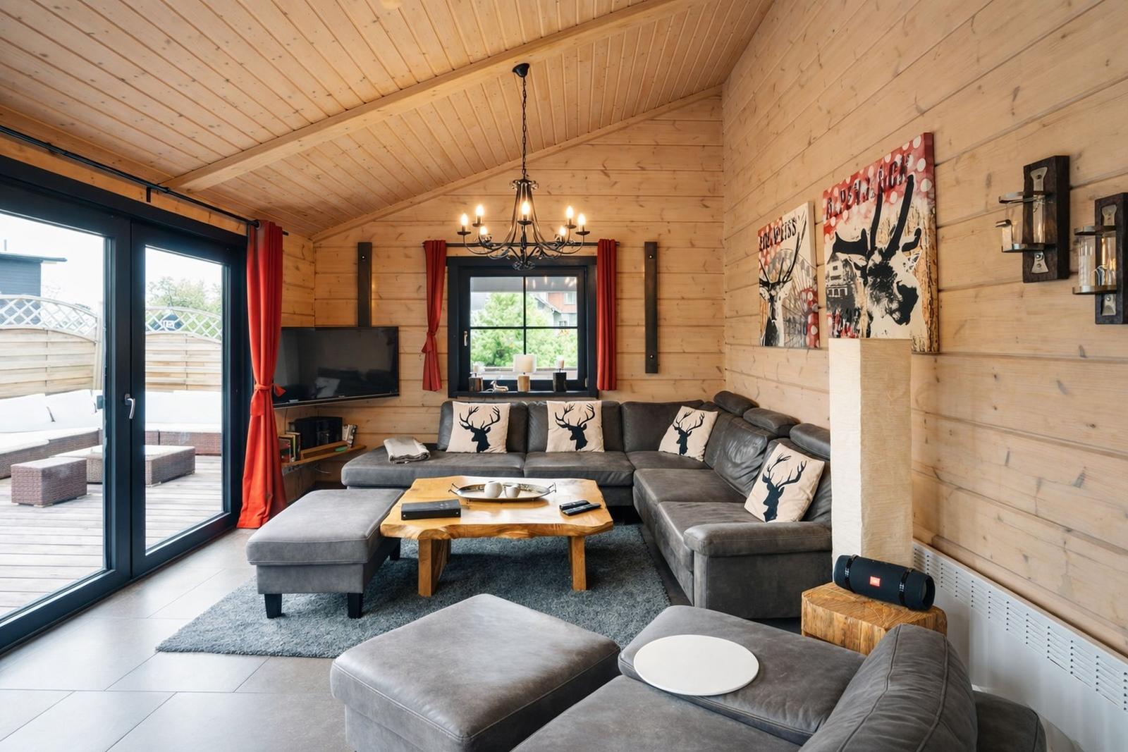 Wohnzimmer mit Holzwand, Sofa, Couchtisch und TV. Terrasse mit Blick draußen.