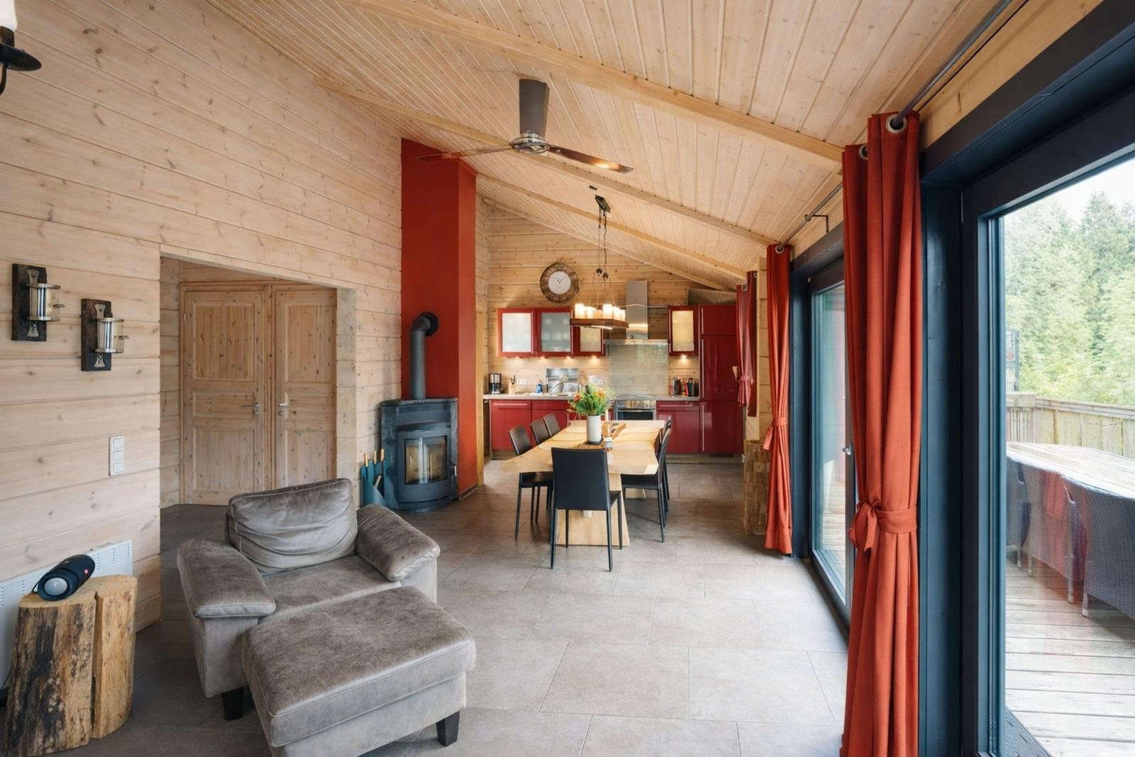 Wohn- und Essbereich mit Holzwand, Kamin und Küchenbereich mit roten Schränken.
