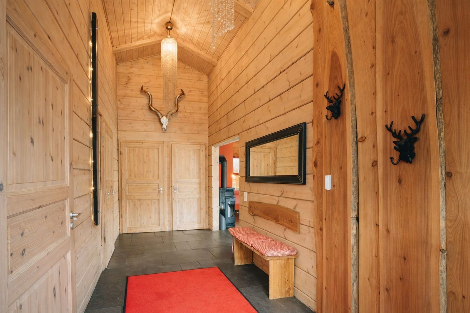 Holzgetäfelte Eingangshalle mit rotem Teppich, Spiegel und Hirschgeweihdekoration.