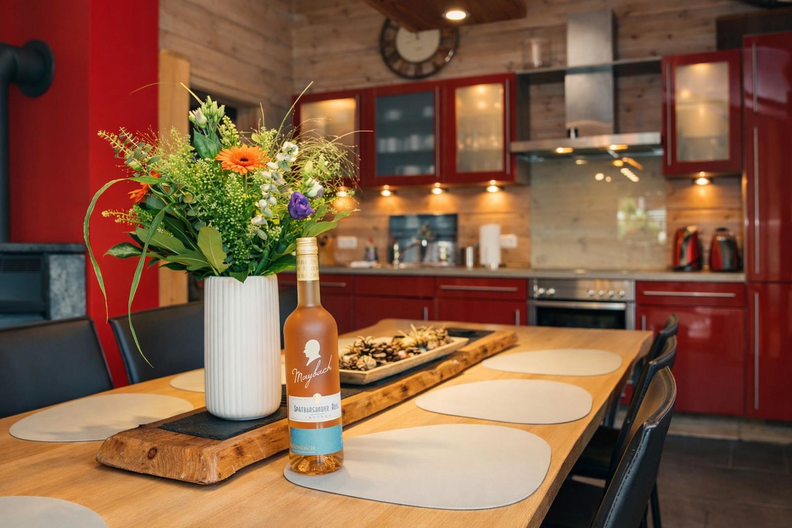 Küche mit roten Schränken und Holztisch. Blumen und Flasche auf Tisch.