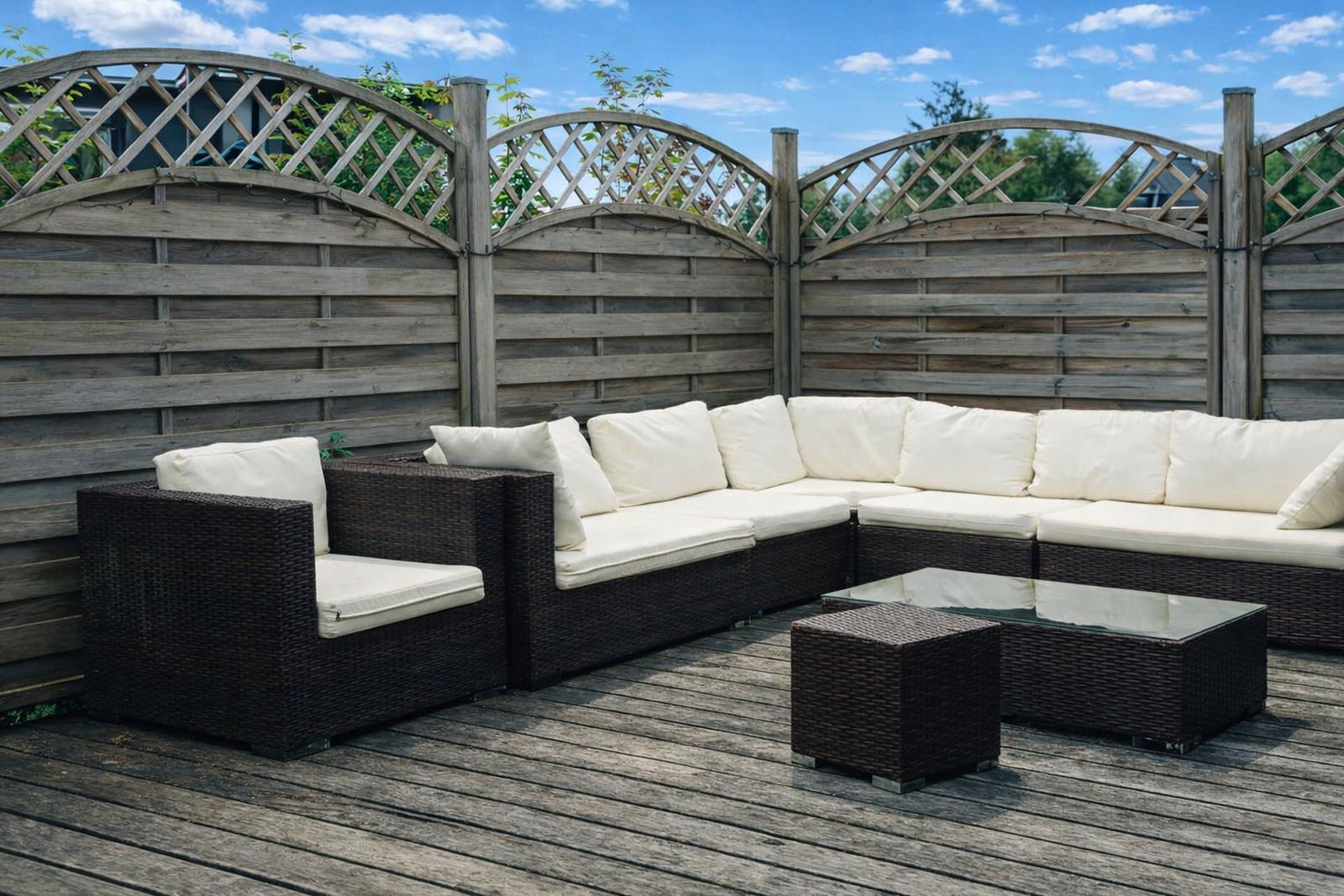Terrasse mit dunkelbraunem Rattan-Sofa und weißen Kissen, Holzgeländer und Holzdecke.
