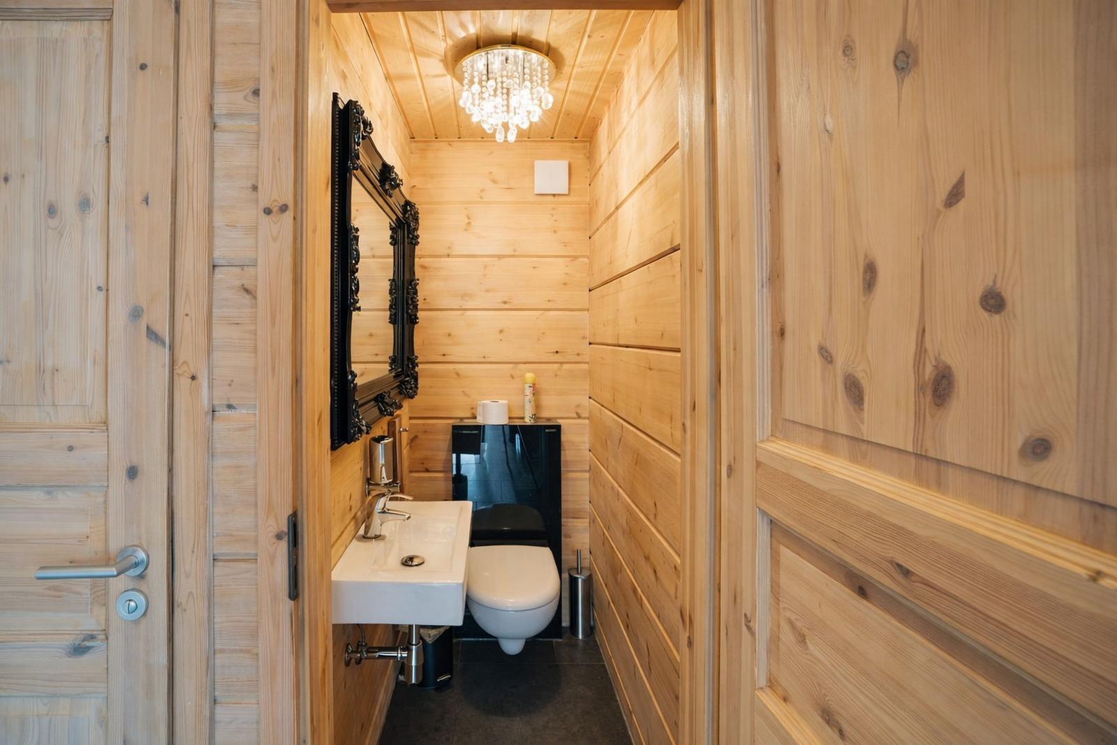 Holzvertäfelte Toilettenkabine mit Spiegel, Waschbecken und Toilette.