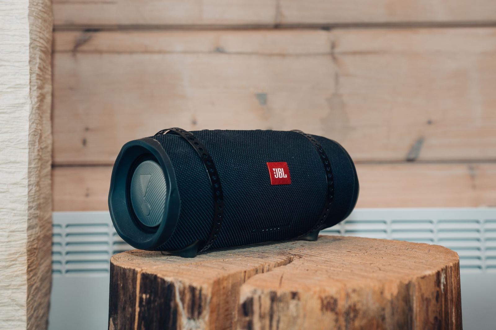 Ein schwarzer JBL-Lautsprecher steht auf einem Holzstück vor einer Holzwand.