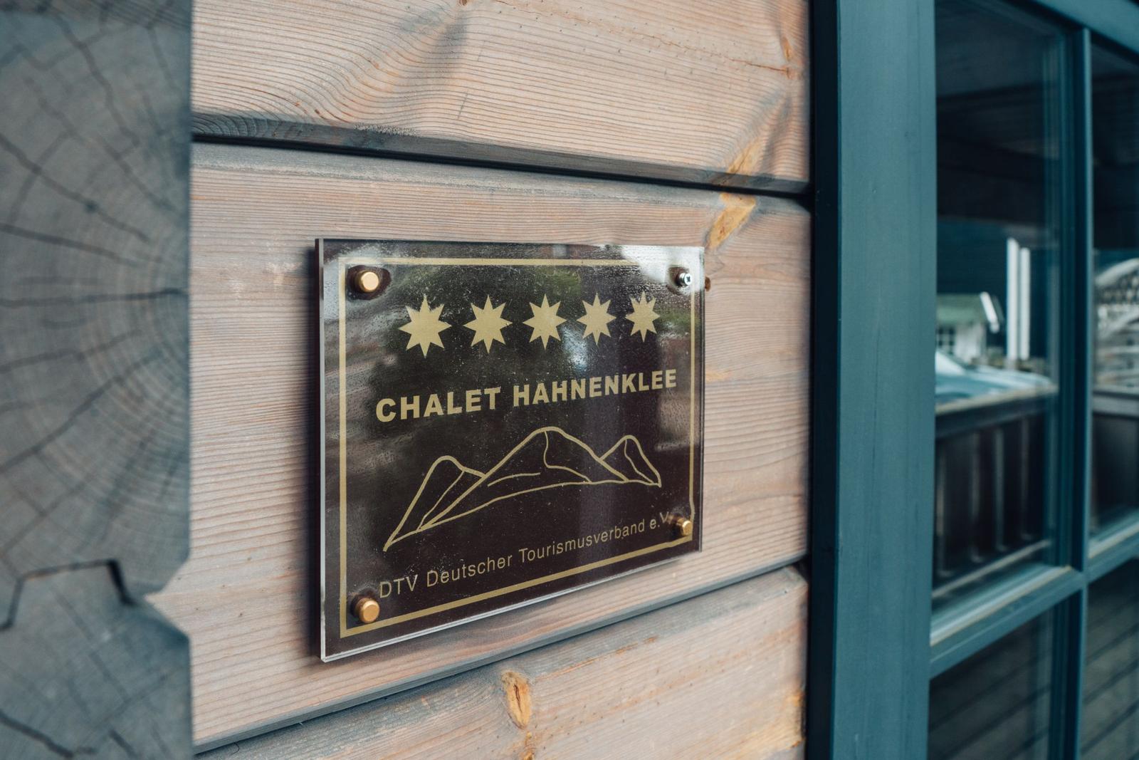 Schild zeigt Chalet Hahnenklee mit fünf Sternen und Bergsymbol. Holzwand und Fenster sichtbar.