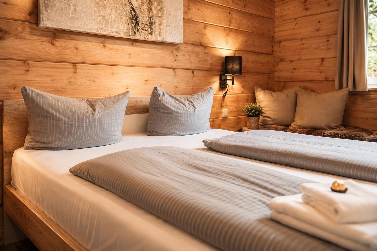 Zwei Betten mit Bettwäsche und Kissen in einem Holzhauszimmer mit Wandbeleuchtung.