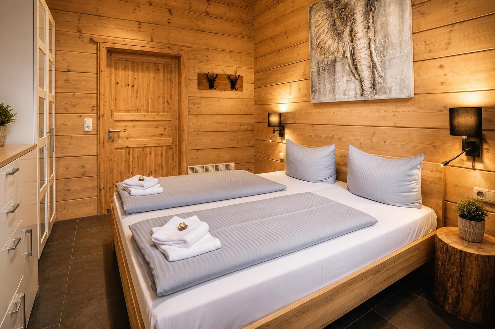 Schlafzimmer mit Holzwand, Bett, Nachttisch und Wandbild.