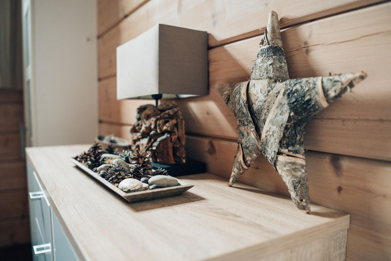 Holzregal mit Stern aus Birke, Lampe und Schale mit Kiefernzapfen und Steinen.