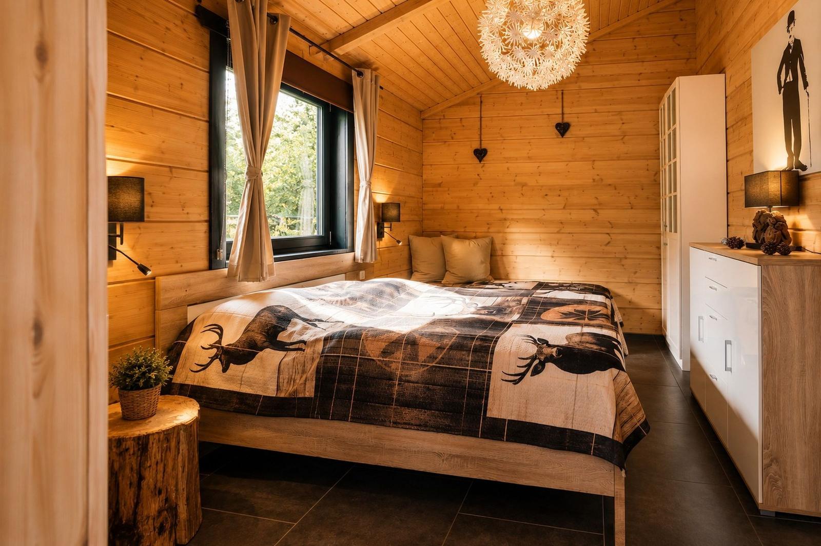 Schlafzimmer mit Holzwand, Bett mit Hirschmuster, Fenster, Schrank und Deckenleuchte.