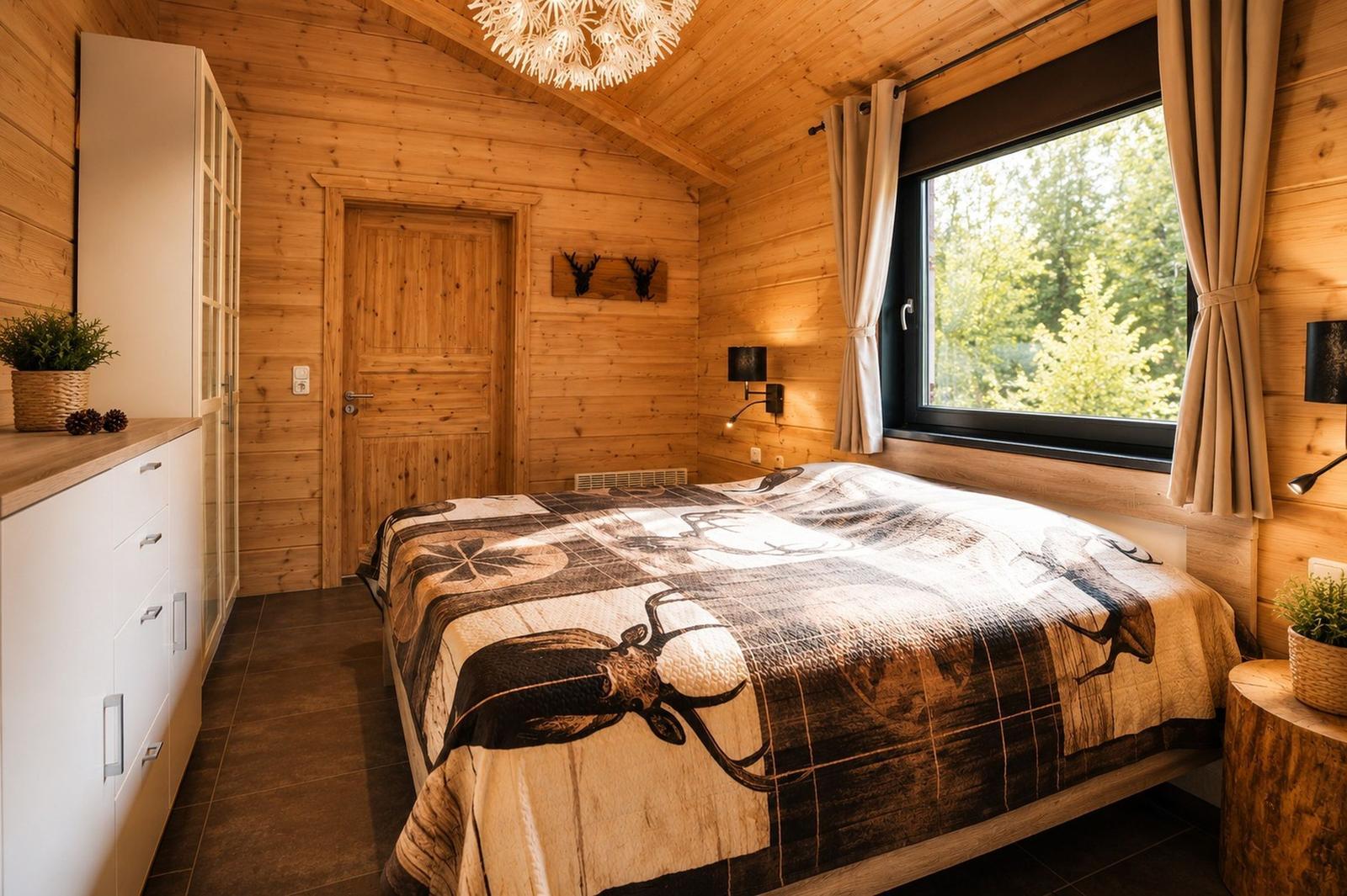 Schlafzimmer mit Holzwand, großem Bett und Fenster mit Blick auf Wald.