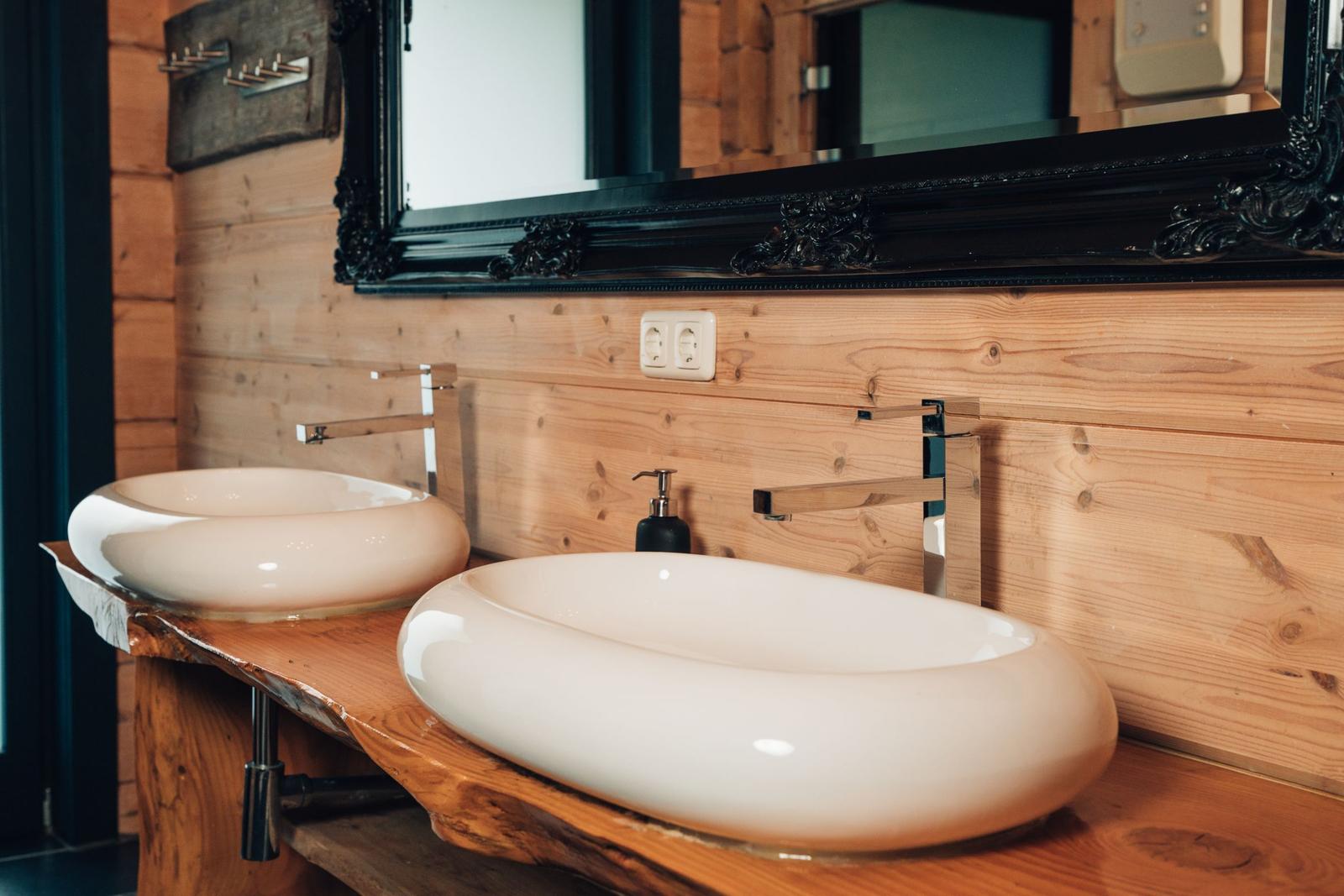 Zwei ovale Waschbecken auf einem Holzunterschrank mit Spiegel darüber.