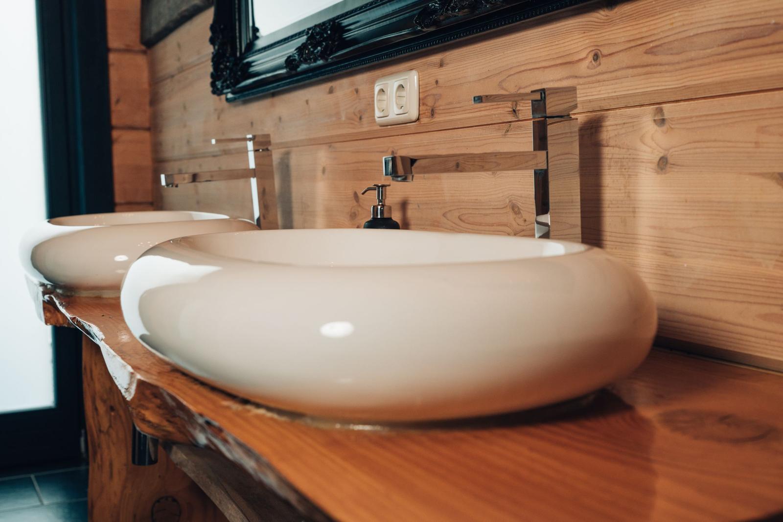 Zwei ovale Waschbecken auf Holzunterlage mit modernen Wasserhähnen und Spiegel darüber.