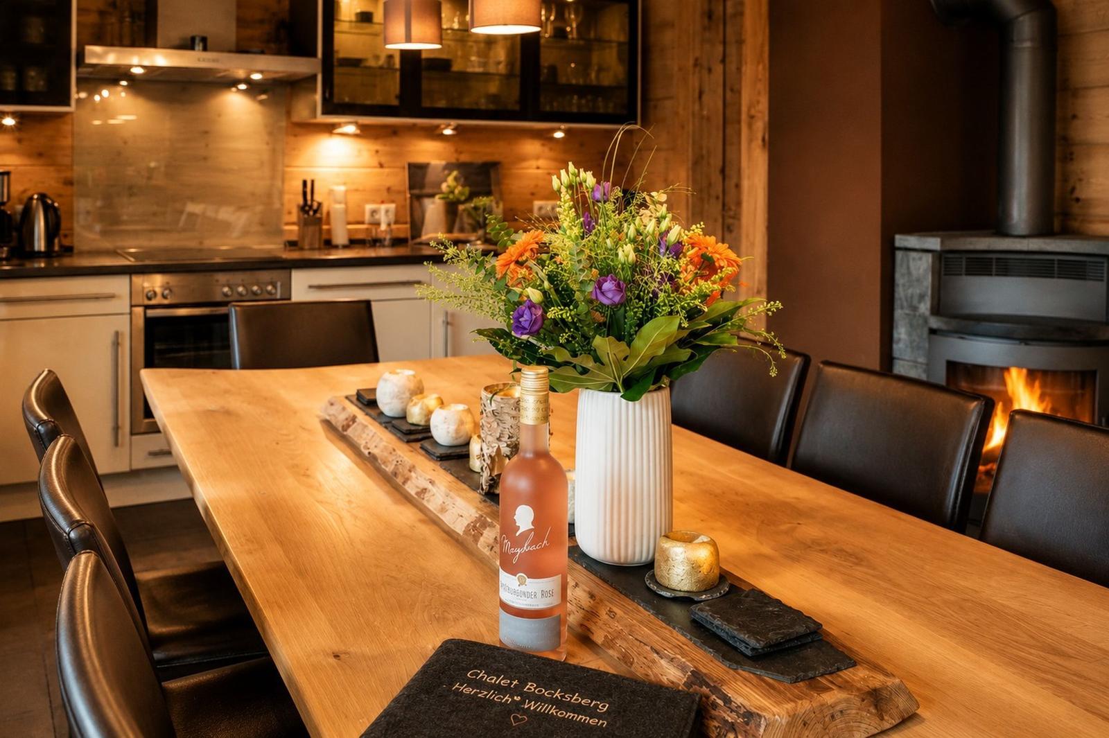 Essbereich mit Holztisch, Blumen und Kamin im Hintergrund.