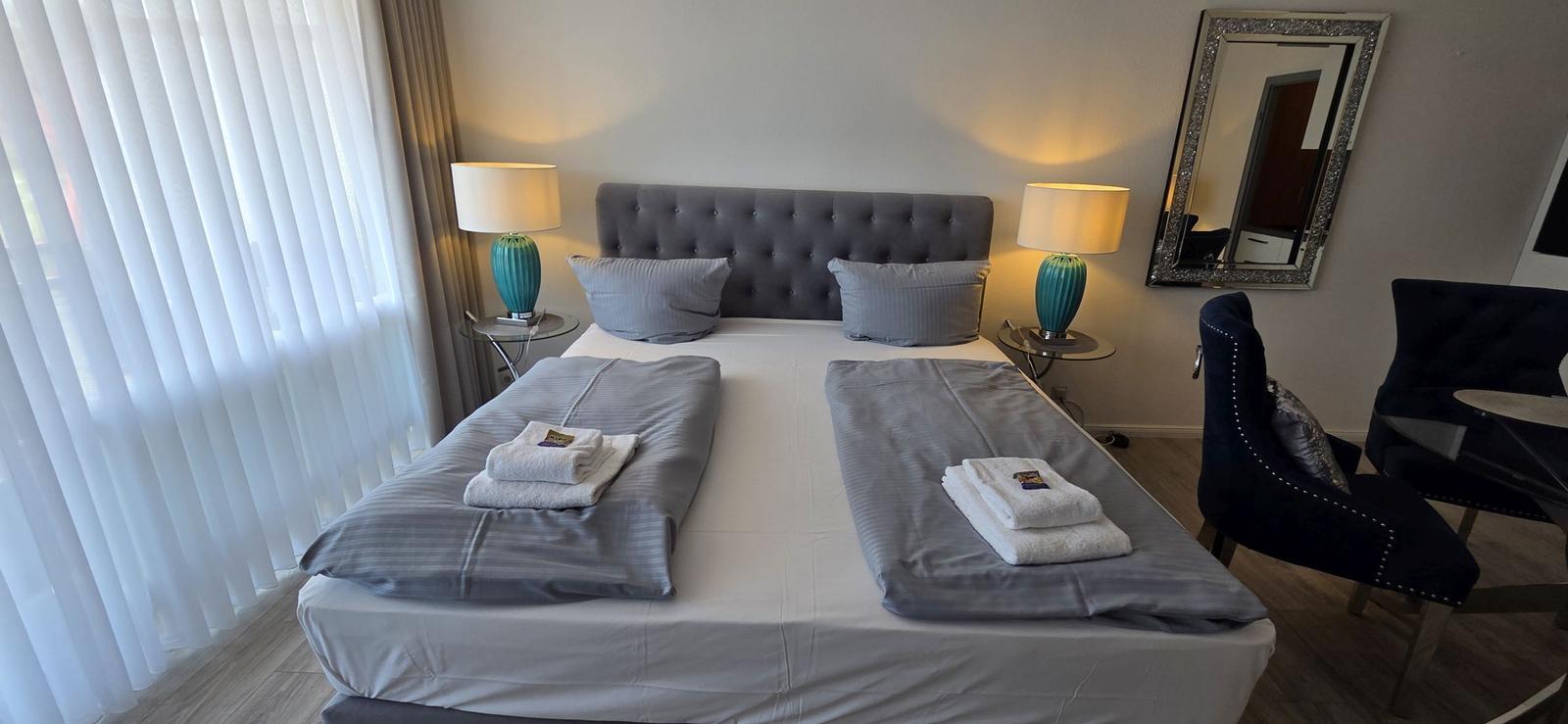 Schlafzimmer mit Doppelbett, zwei Nachttischen, Spiegel und Stühlen.