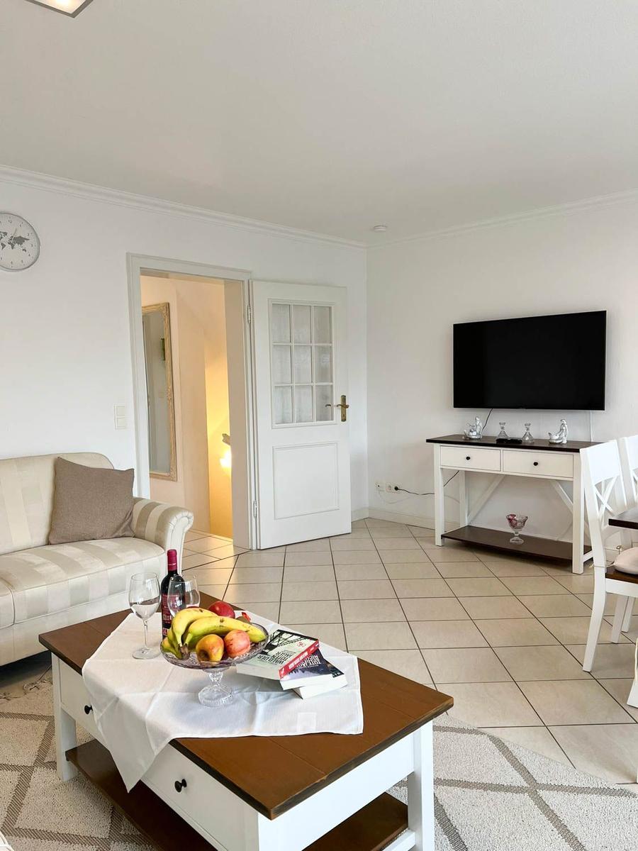 Wohnzimmer mit Sofa, Fernseher und Esstisch mit Obst und Wein.