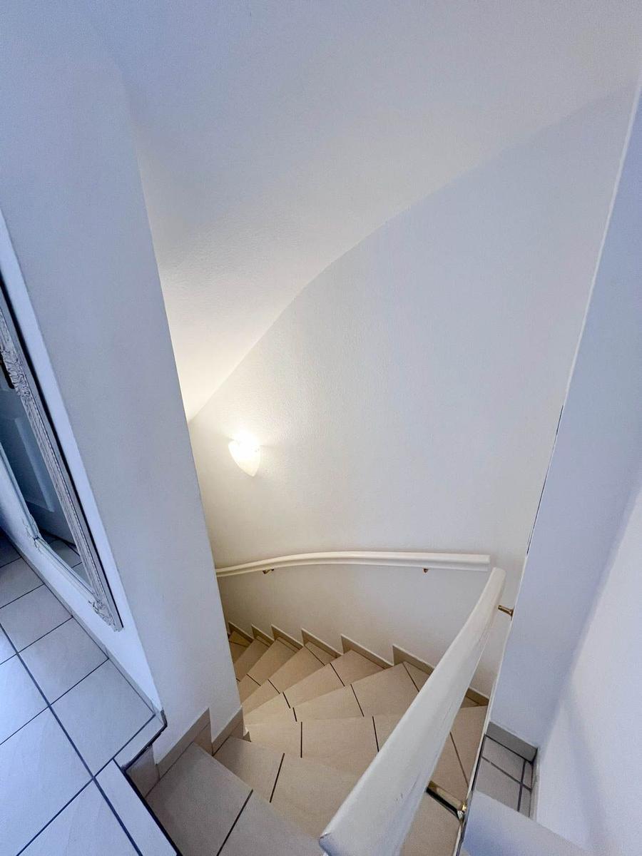 Helle Treppe mit Handlauf und Wandbeleuchtung führt nach oben.