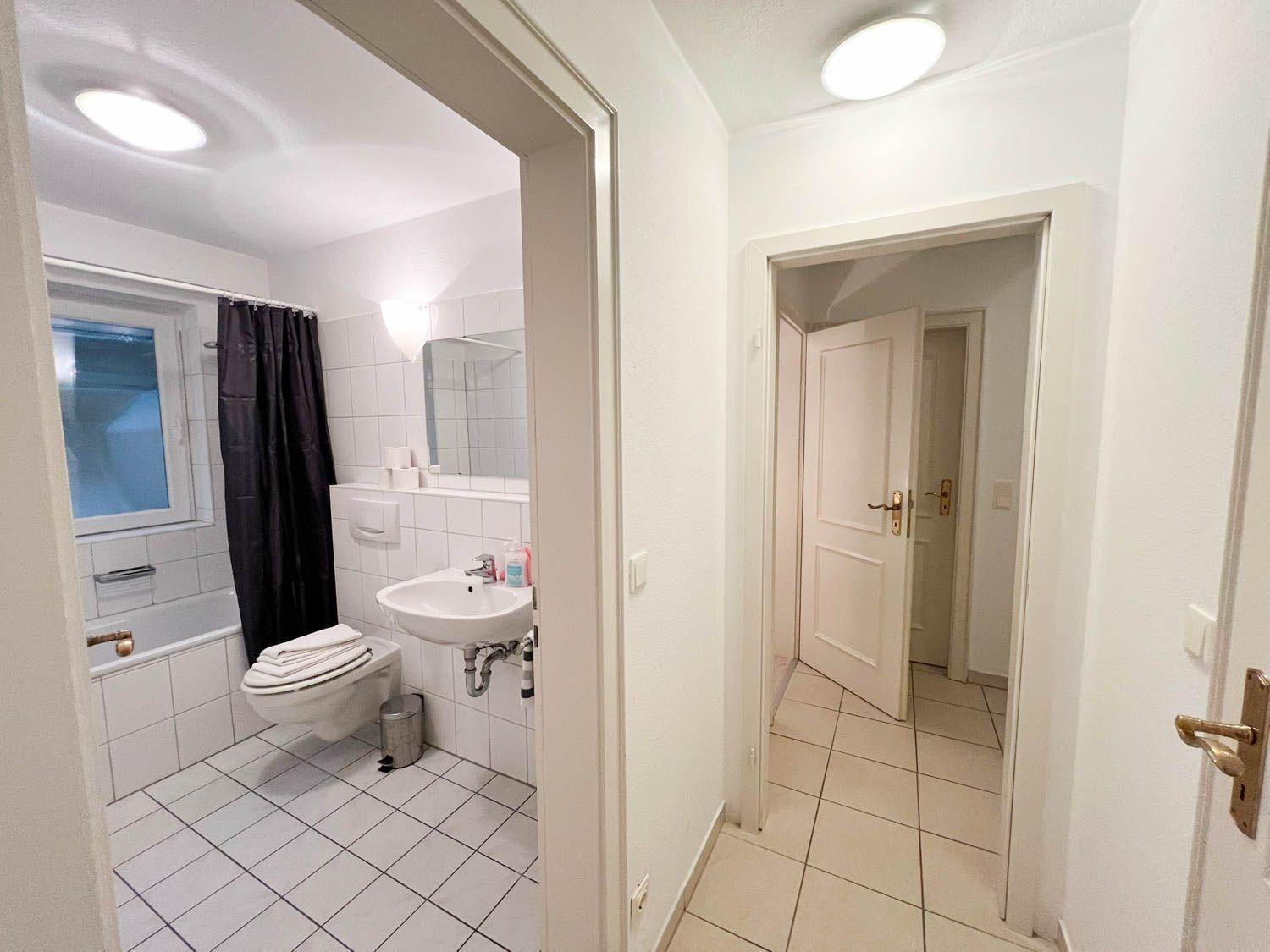 Badezimmer mit Dusche, Waschbecken und Toilette. Flur führt in weitere Räume.