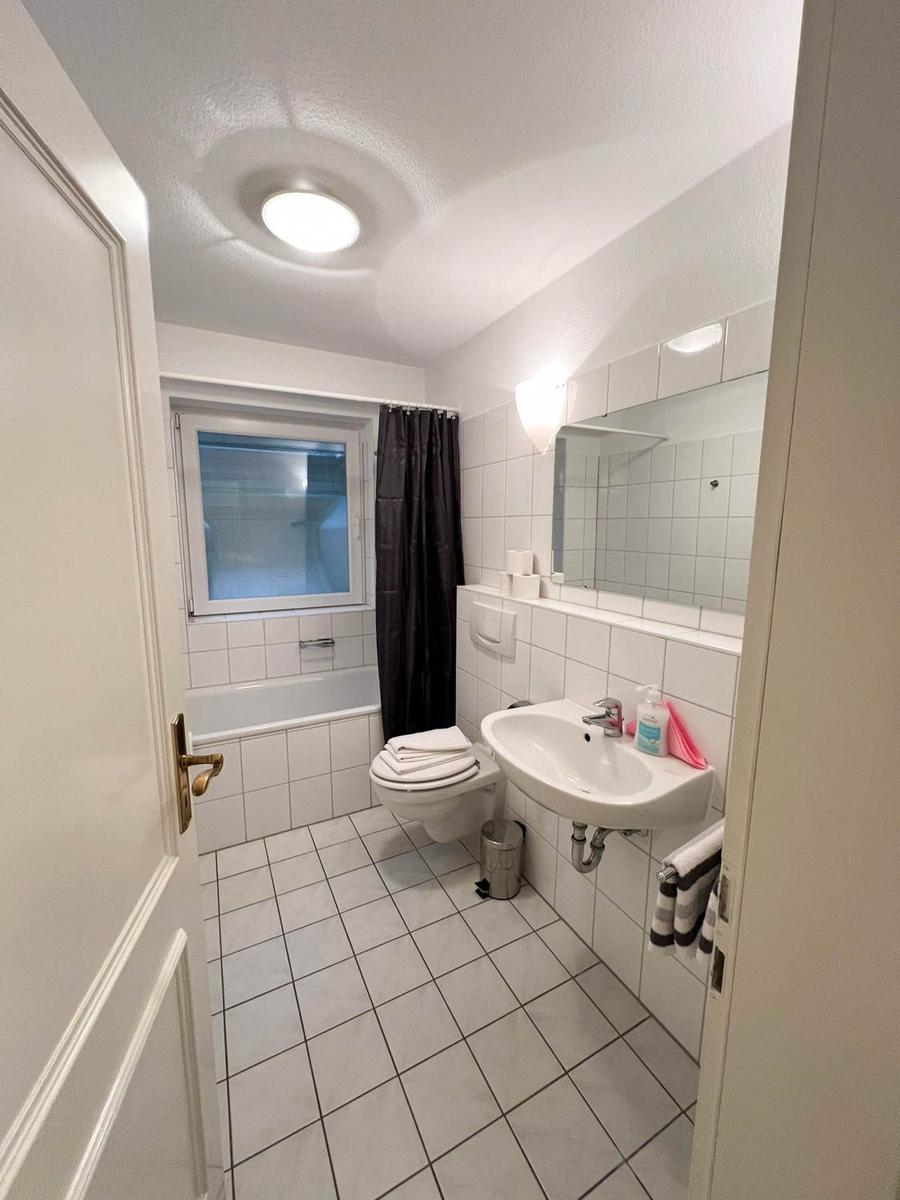 Badezimmer mit Badewanne, Toilette und Waschbecken. Fenster mit Vorhang.
