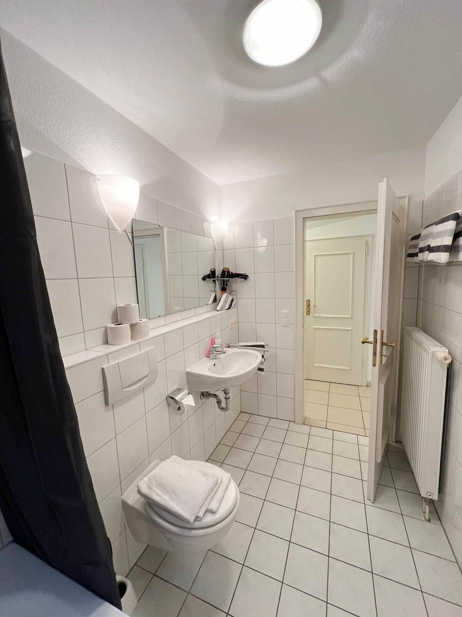 Badezimmer mit Toilette, Waschbecken und Dusche. Weiße Fliesen und Spiegel.