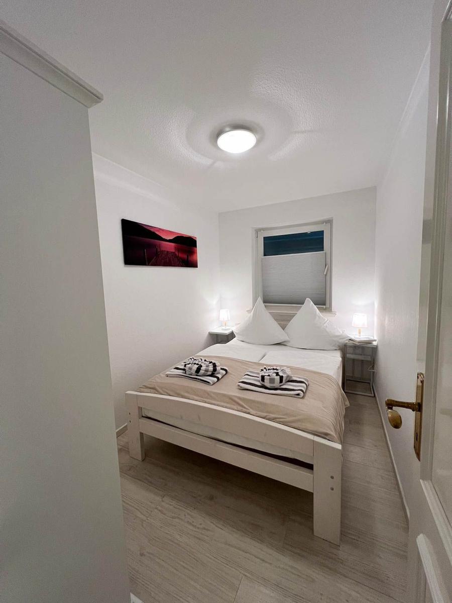 Schlafzimmer mit Bett, Nachttischen und Wandbild. Holzfußboden und Fenster mit Jalousie.