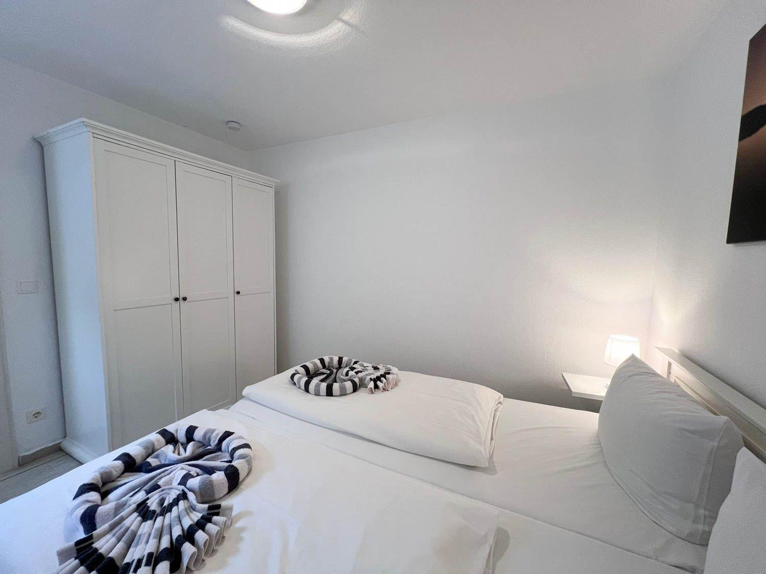 Schlafzimmer mit weißem Bett, Kleiderschrank und Nachttisch mit Lampe.