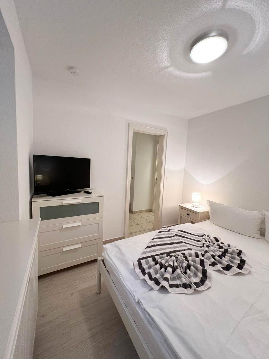 Schlafzimmer mit Bett, Nachttisch, Fernseher und Schrank. Tür führt in angrenzenden Raum.