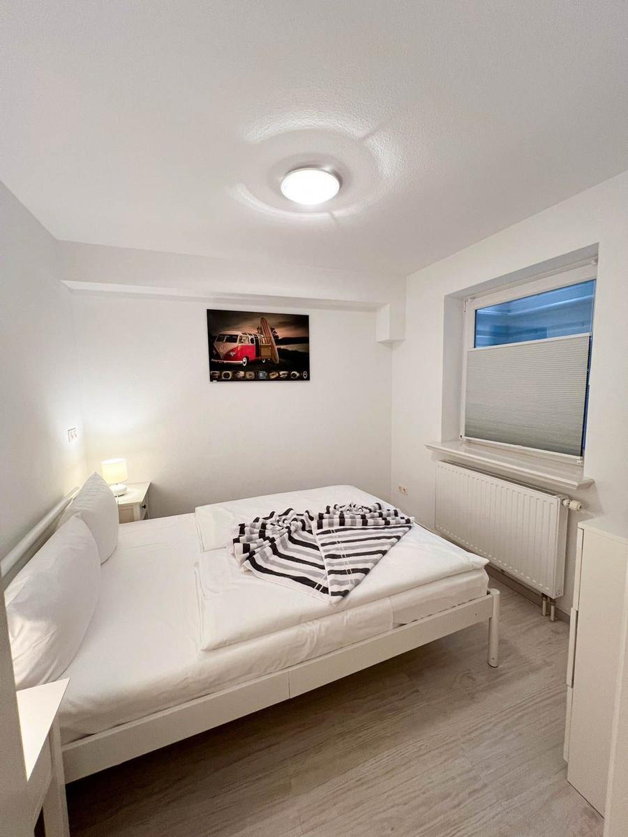 Schlafzimmer mit weißem Bett, Wandbild und Fenster mit Jalousie.