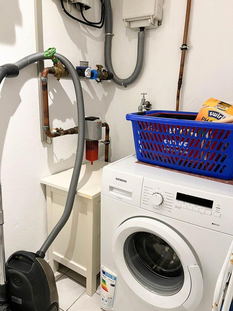Waschmaschine mit blauem Korb und Rohrleitungen an der Wand