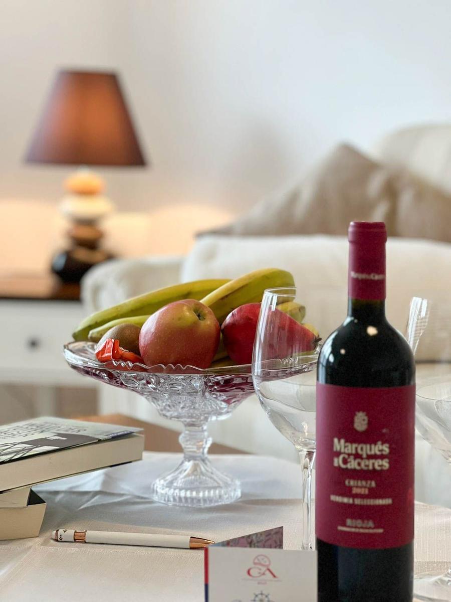 Tisch mit Weinflasche, Obstschale und Glas. Im Hintergrund Lampe und Sofa.