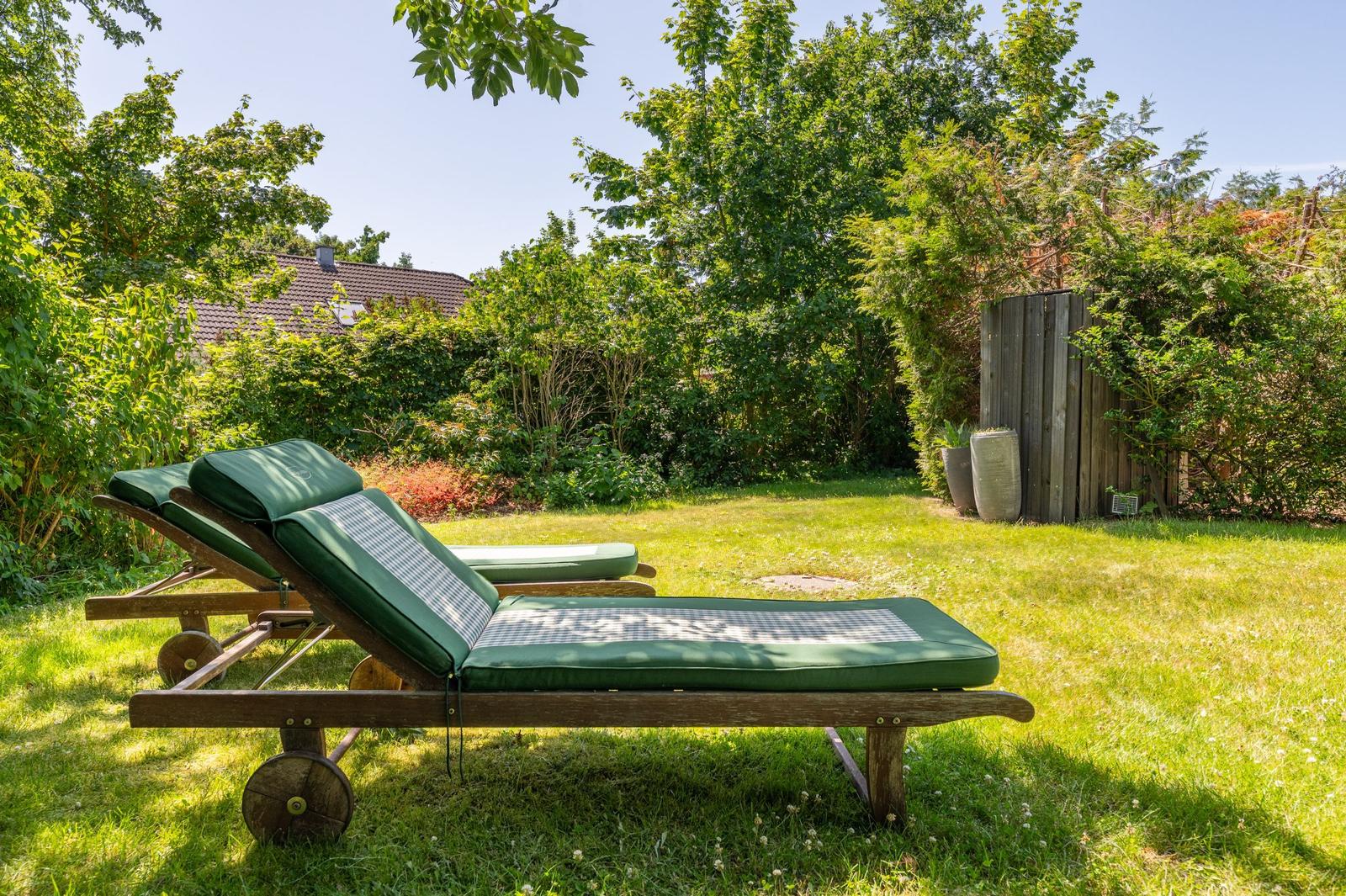 Zwei grüne Liegestühle stehen auf einer Wiese im Garten.