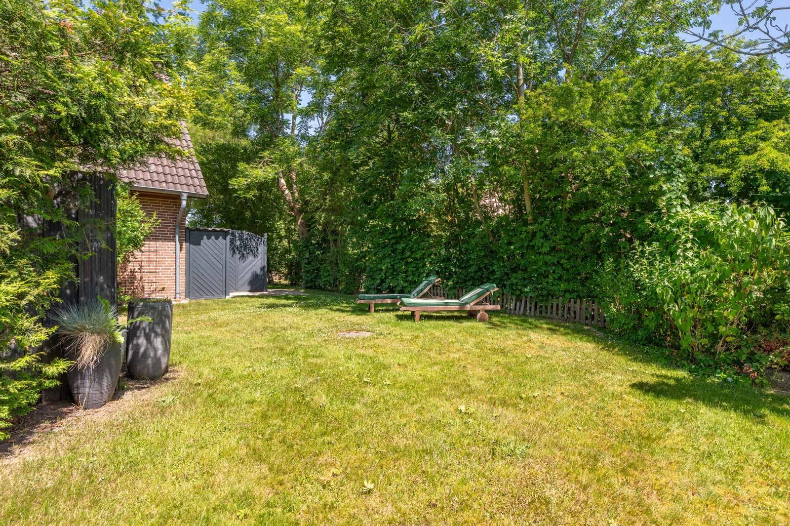 Hinterhof mit grünem Rasen, Liegestühlen und Bäumen. Links steht ein kleines Gebäude.