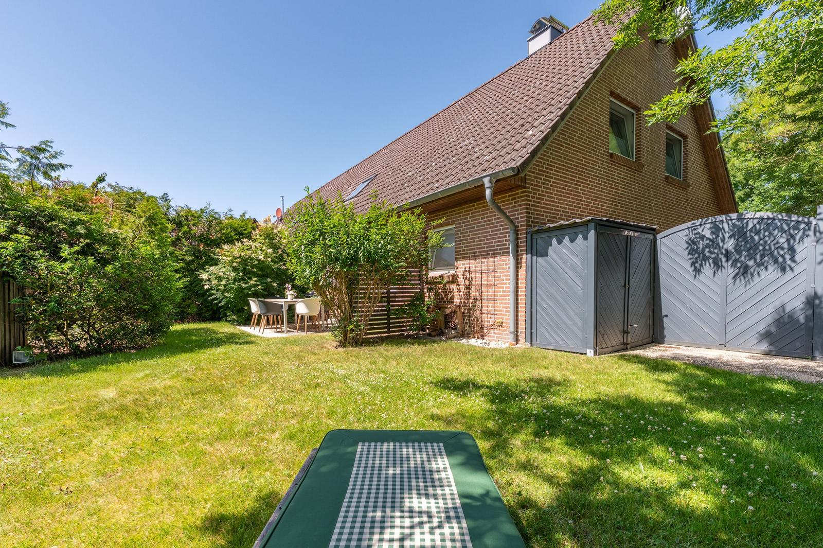 Hinterhof mit Garten, Tisch, Gartenmöbel und Terrasse. Haus mit Ziegeldach und Garagen.