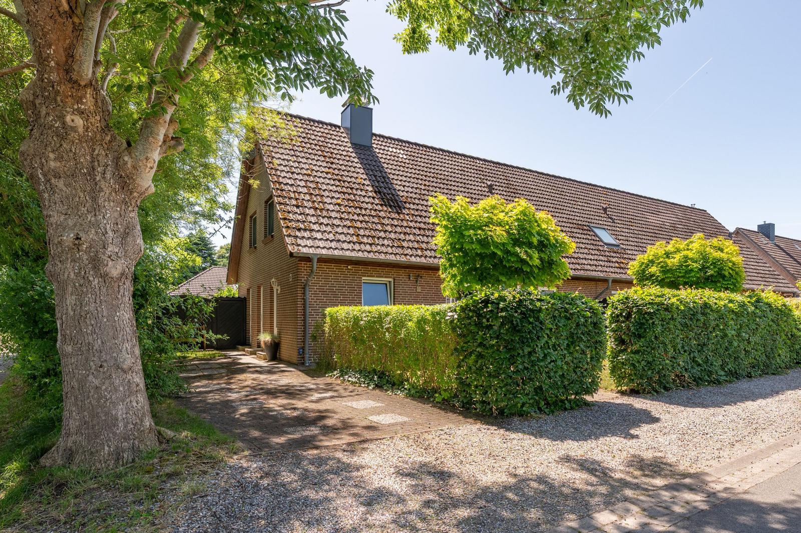 Ein zweistöckiges Haus mit Ziegeldach, umgeben von grünen Büschen und einem großen Baum.