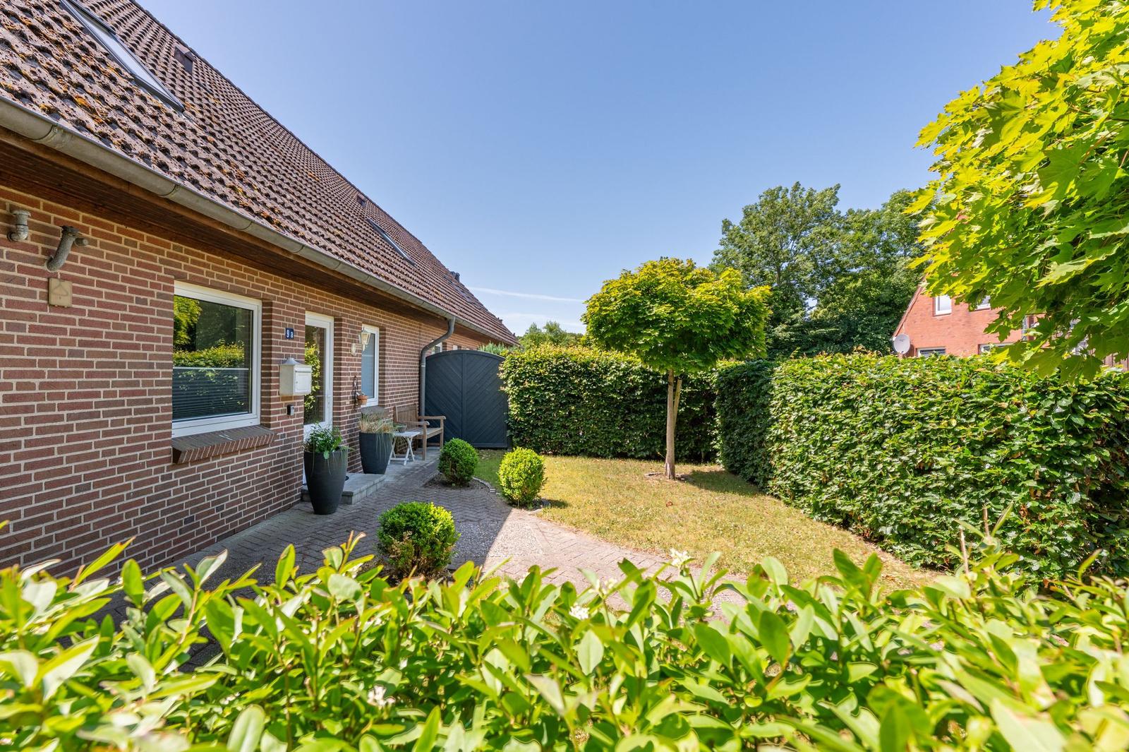 Haus mit Garten, Hecke und Baum unter blauem Himmel.