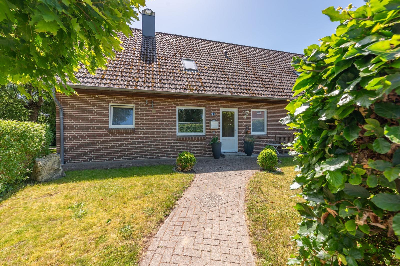 Ein Einfamilienhaus mit Backsteinfassade und Schieferdach. Ein gepflasterter Weg führt zur Eingangstür.