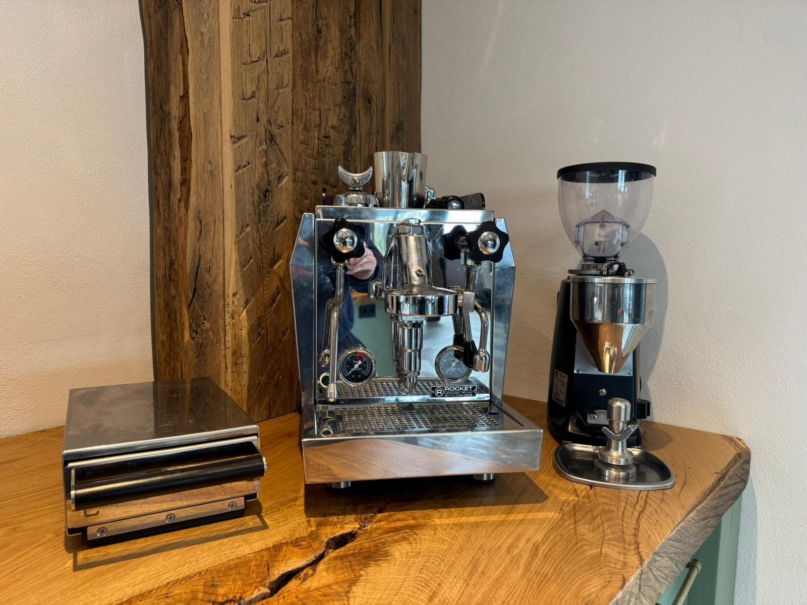 Kaffeebereitungseinrichtung auf Holztisch mit Espressomaschine, Mahlwerk und Waage.
