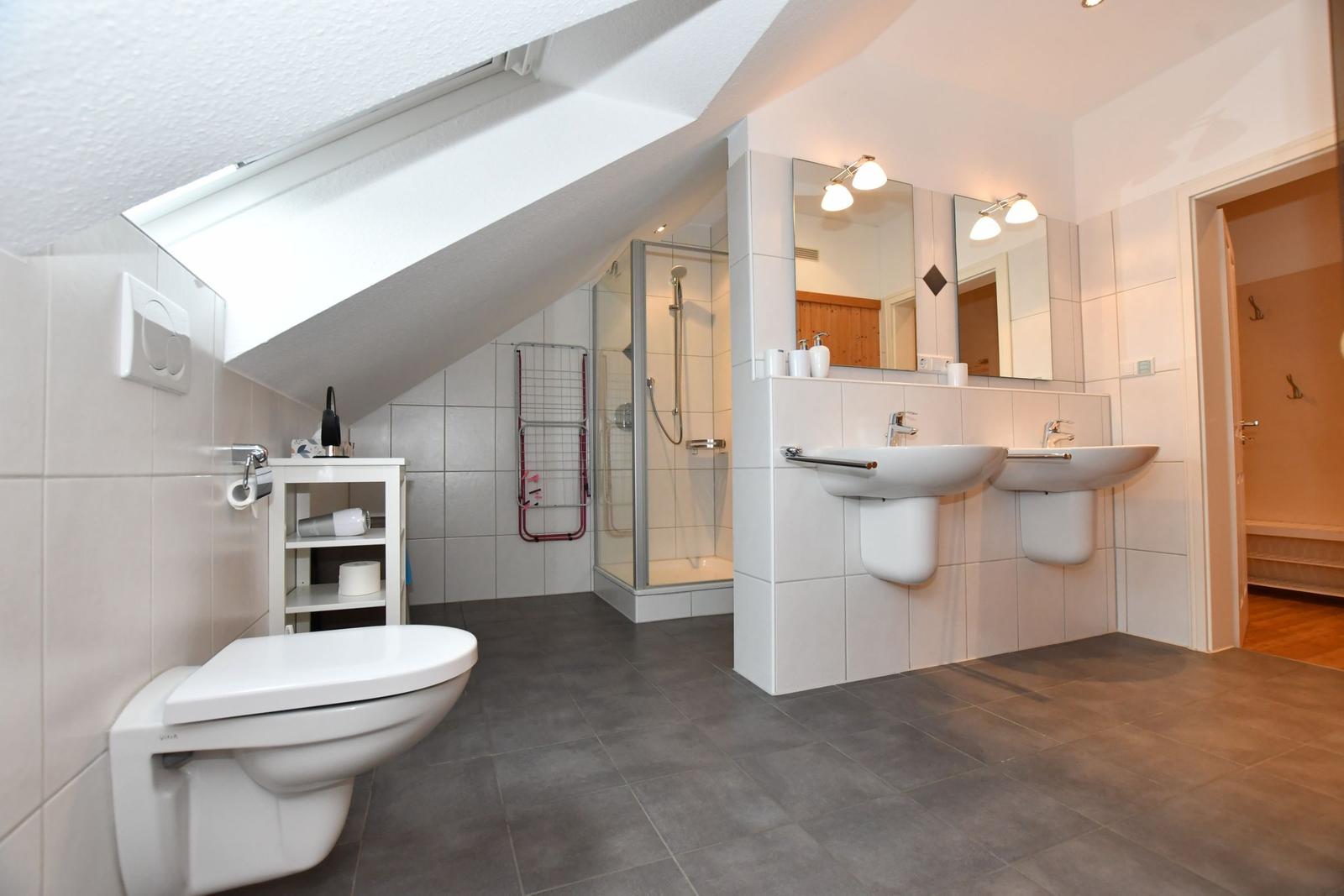 Badezimmer mit Dusche, zwei Waschbecken und Toilette unter Dachschrägen.