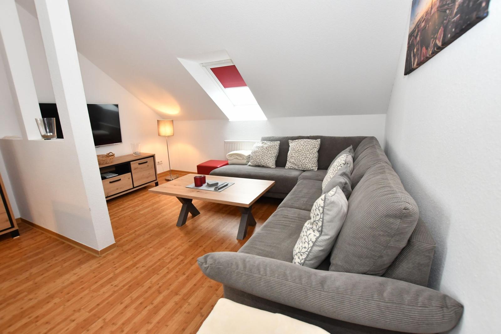 Wohnzimmer mit grauem Sofa, Holzboden und Dachfenster.