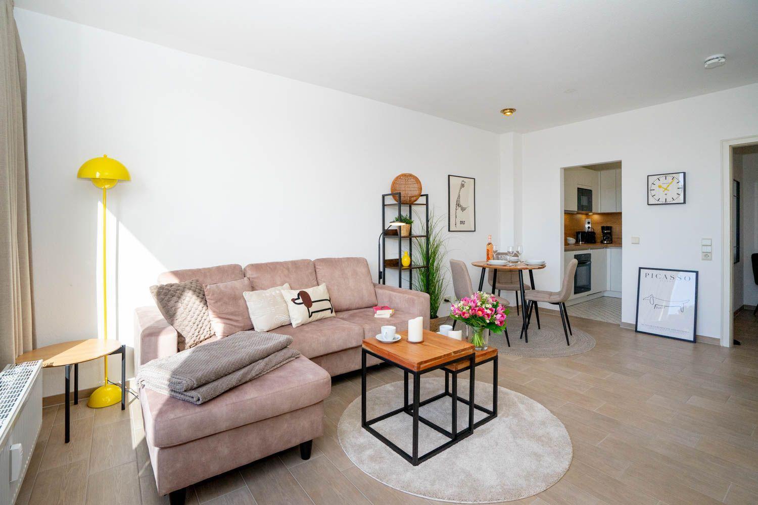 Wohnzimmer mit Sofa, Tisch und Küchenbereich im Hintergrund.