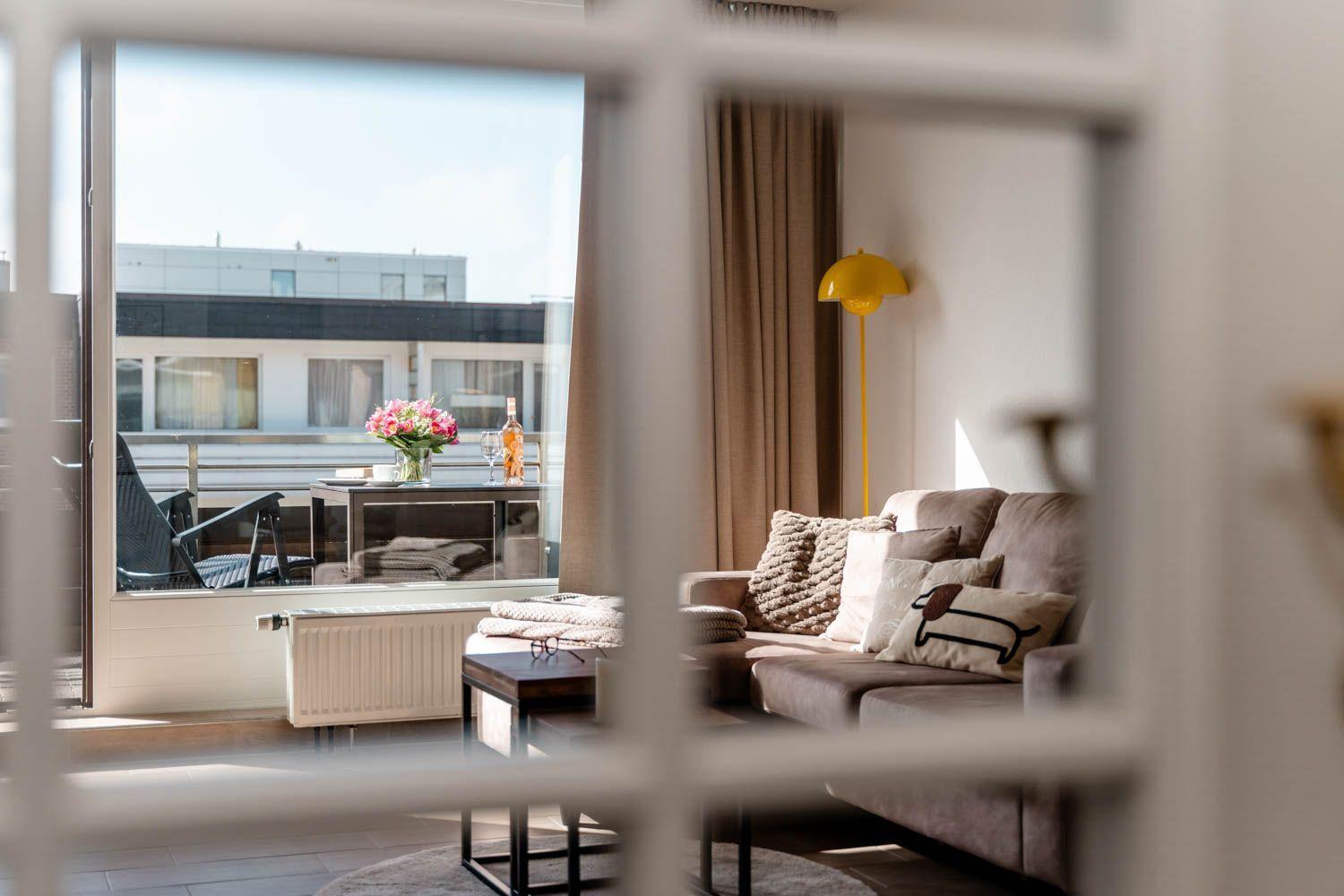 Wohnzimmer mit Sofa, Couchtisch und Balkon. Gelbe Stehlampe und Blumen auf Tisch.