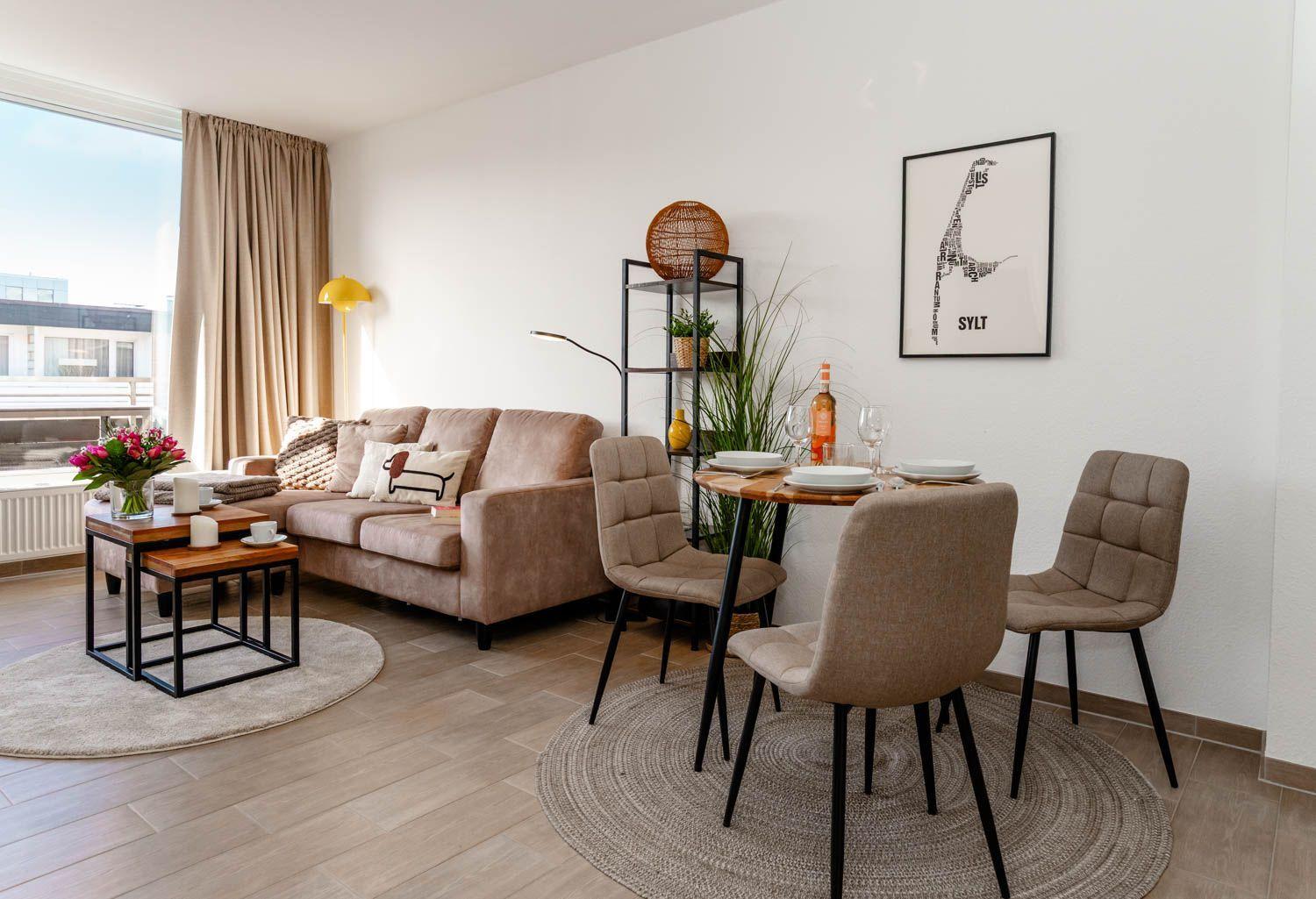 Wohn- und Essbereich mit Sofa, Tisch und Stühlen. Fenster mit Vorhang. Wandbild Sylt.