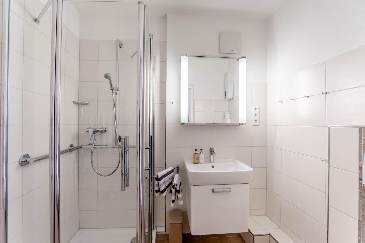 Badezimmer mit Dusche, Waschbecken und Spiegel.