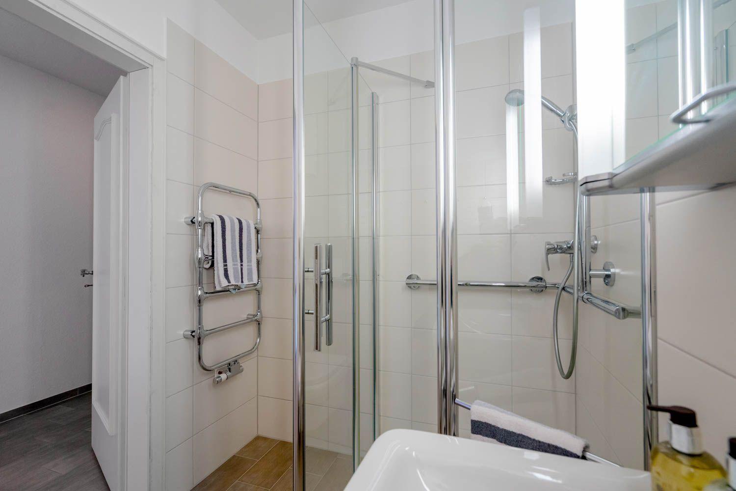 Badezimmer mit Dusche, Handtuchhalter und Waschbecken.