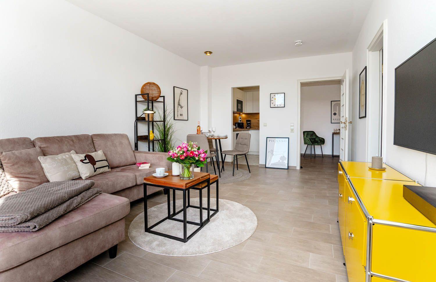 Wohnzimmer mit Sofa, Couchtisch und gelbem Schrank. Küche und Schlafzimmer sind sichtbar.