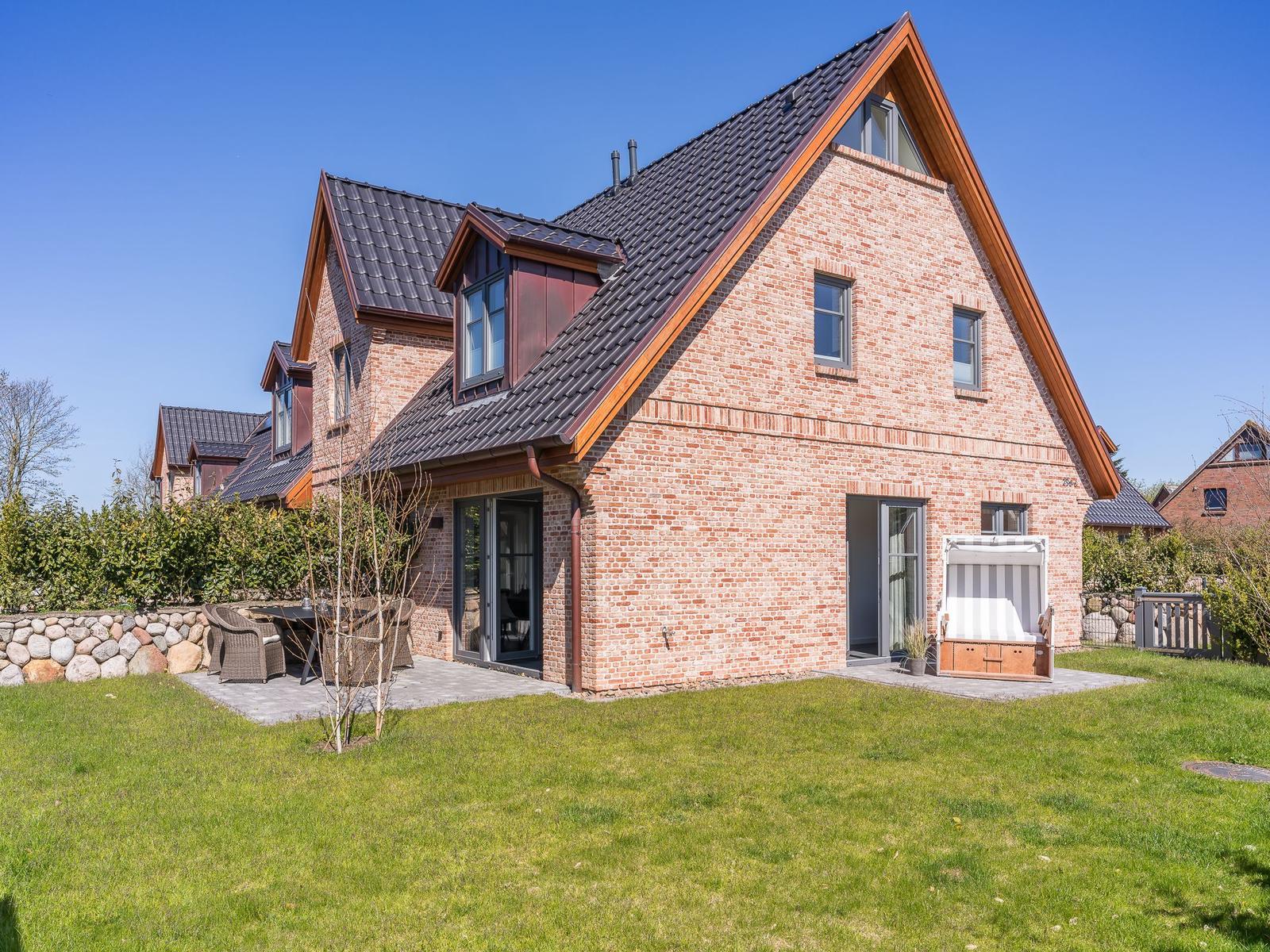 Haus mit Backsteinfassade, Terrasse und Garten. Holzrahmen und dunkle Dachziegel.