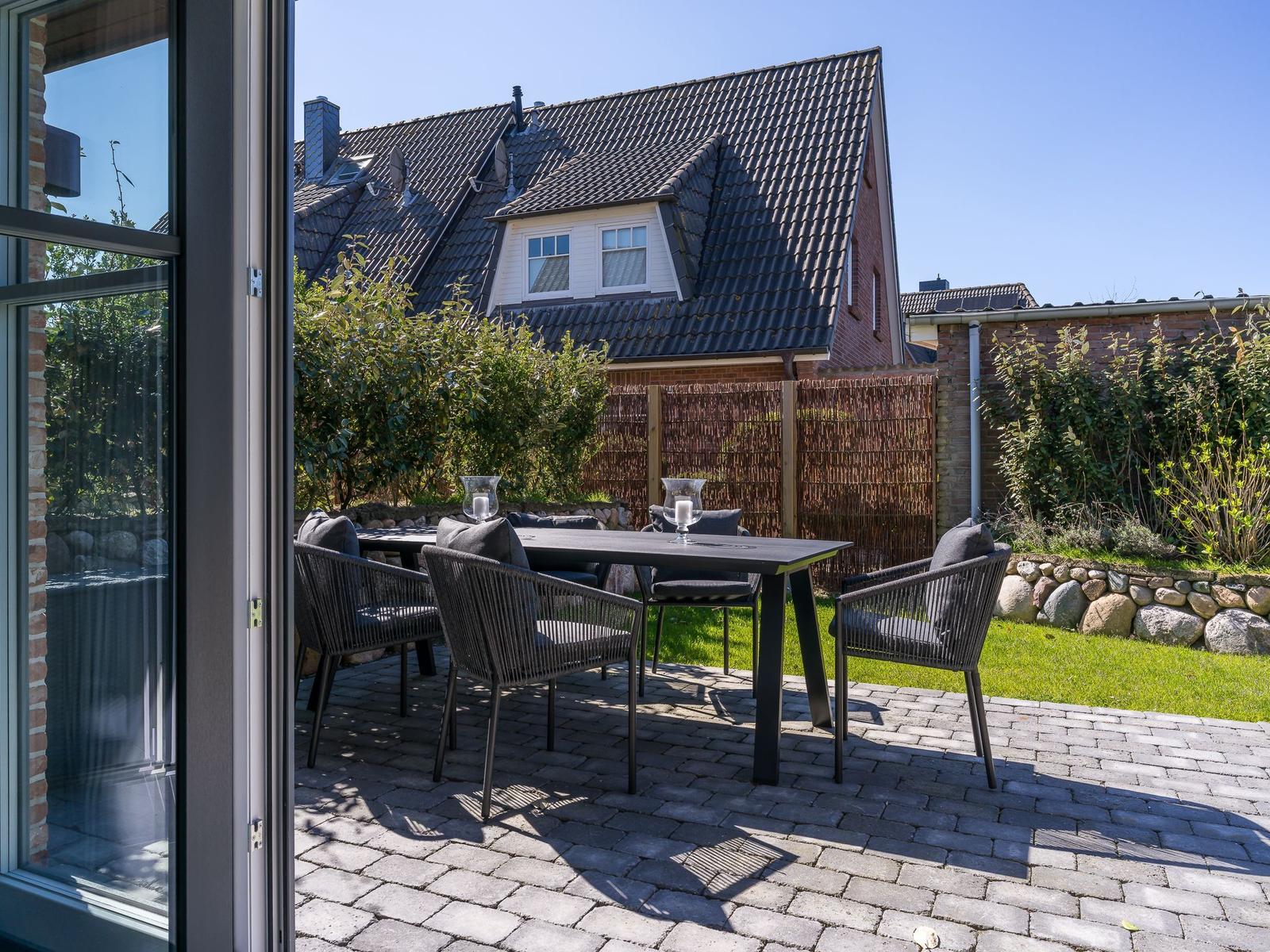 Terrasse mit Tisch und Stühlen, umgeben von Grün und Steinmauer.