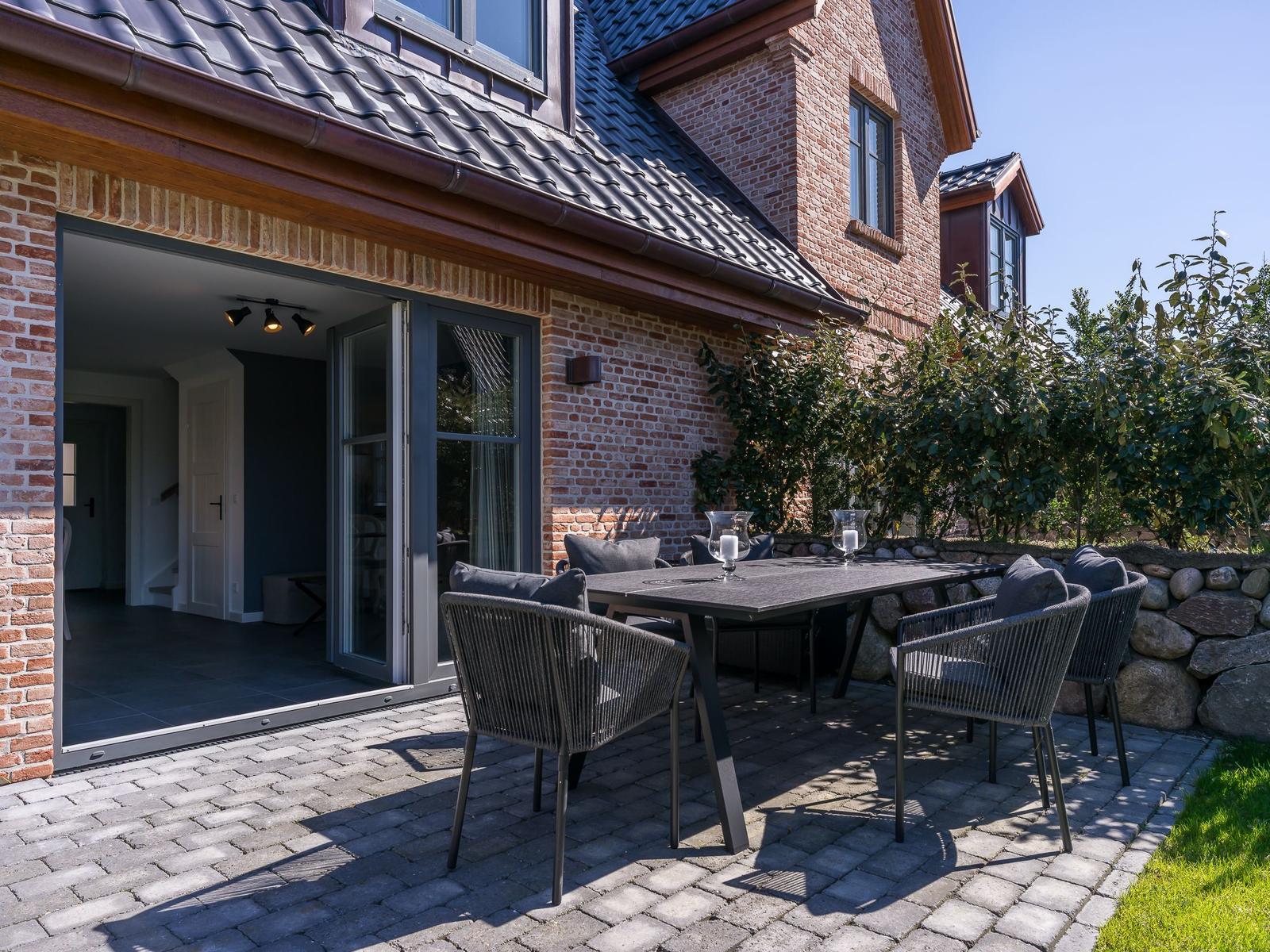 Terrasse mit Tisch und Stühlen vor einem Haus mit Backsteinfassade und offener Tür.