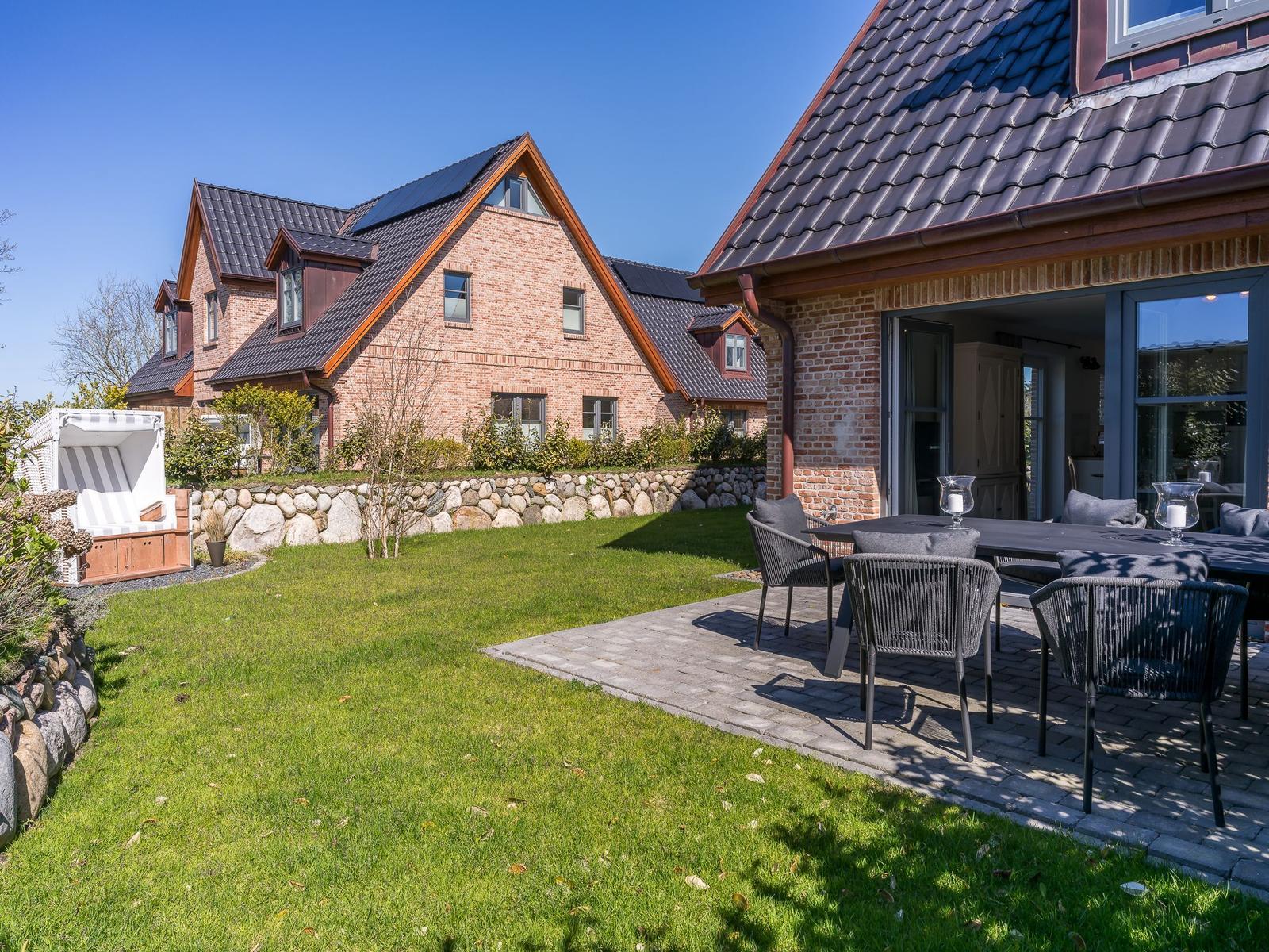 Haus mit Garten, Terrasse und Essbereich. Steinmauer, Grasfläche und Sonnenschutz.