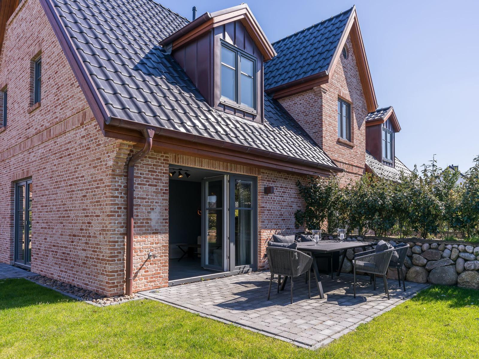 Haus mit Terrasse, Tisch und Stühlen, umgeben von Gras und Steinmauer.