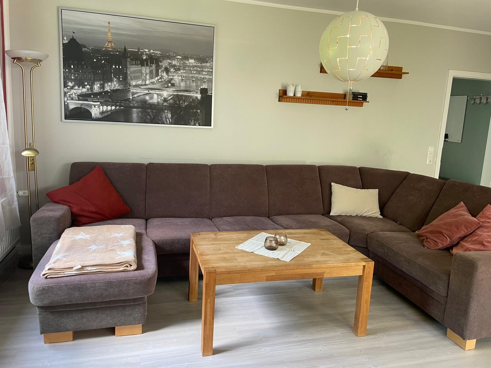 Ein Wohnzimmer mit braunem Sofa, Holztisch und Wandbild von Paris.